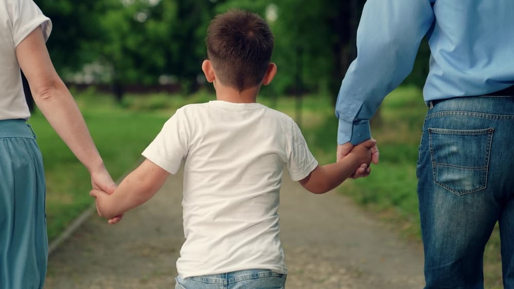 Child son walks with mom dad in park holding hands.